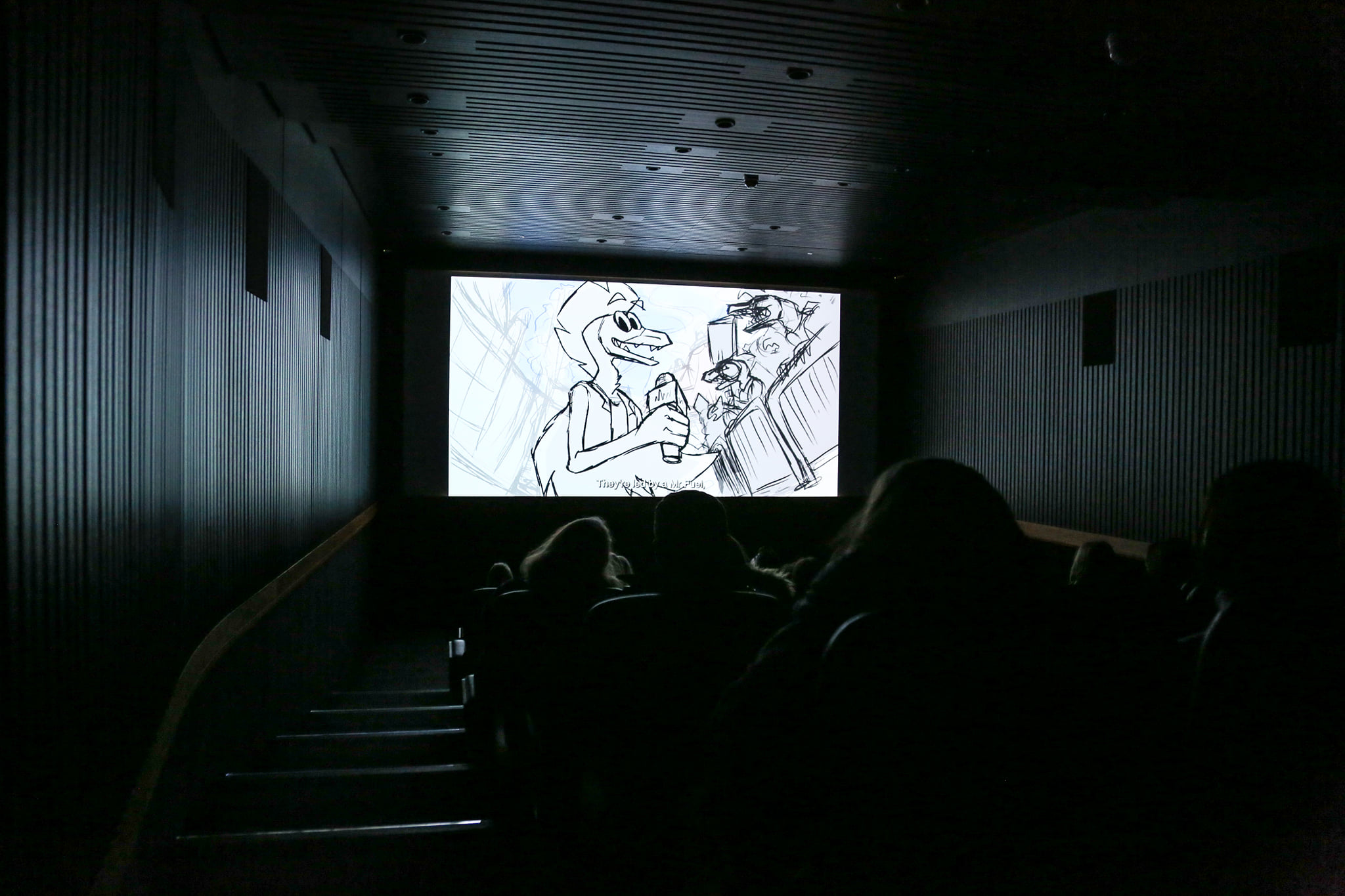 A dark cinema room with a lit screen with an animated film. The outlines of some heads in the audience can be seen, lit by the screen.
