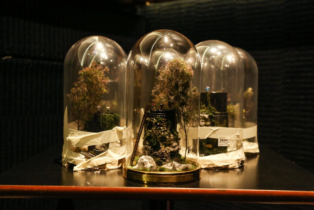Three trophies made of a glass case with an up-cycled lens and vegetation and figures inside them.